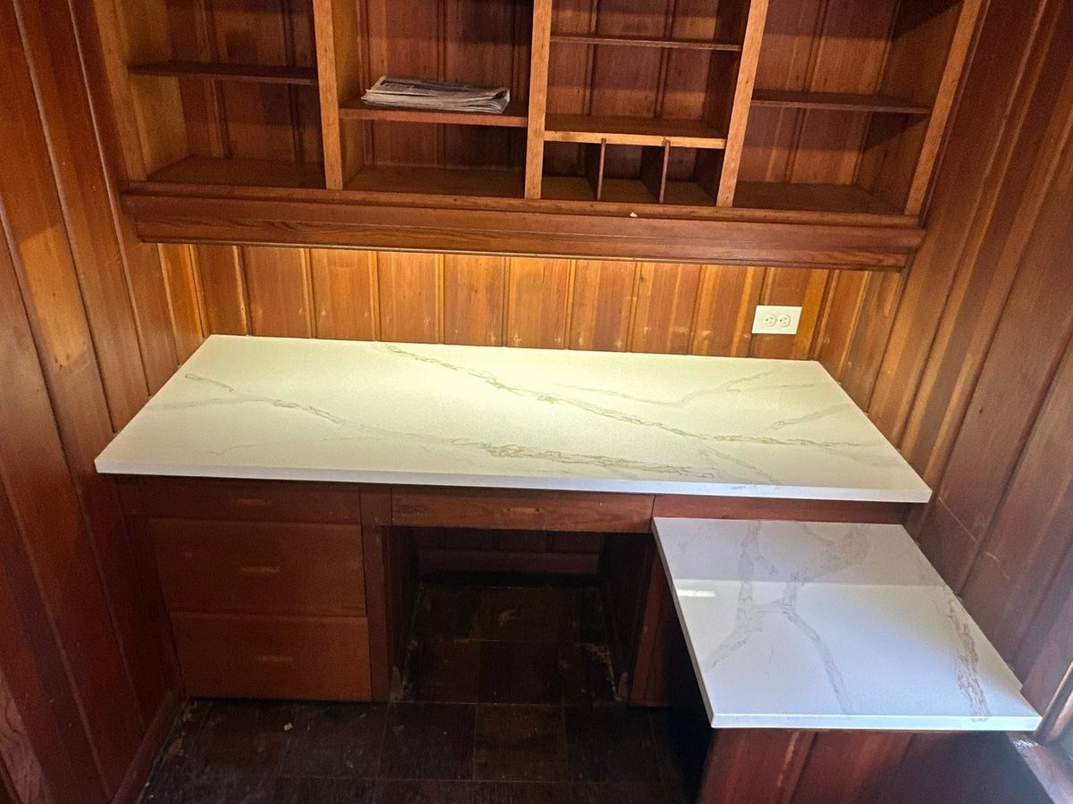 Built-in desk topped with white veined stone against wood paneling.