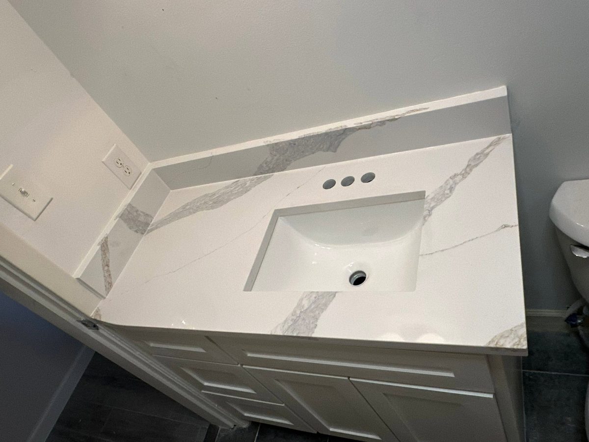 Bathroom vanity with a white and gold veined stone top and matching backsplash.