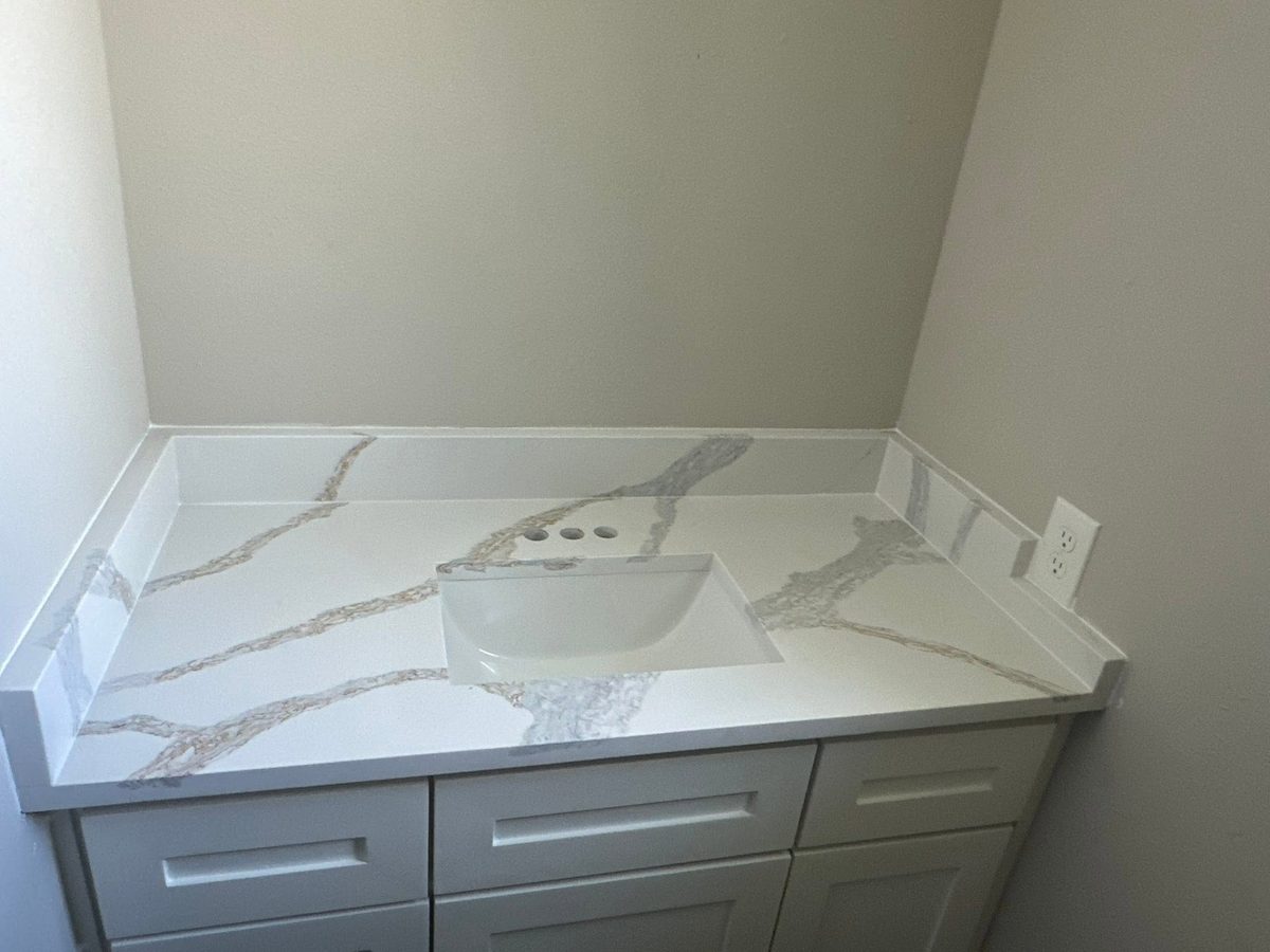 Powder room vanity top in white and gold veined stone with a side splash.