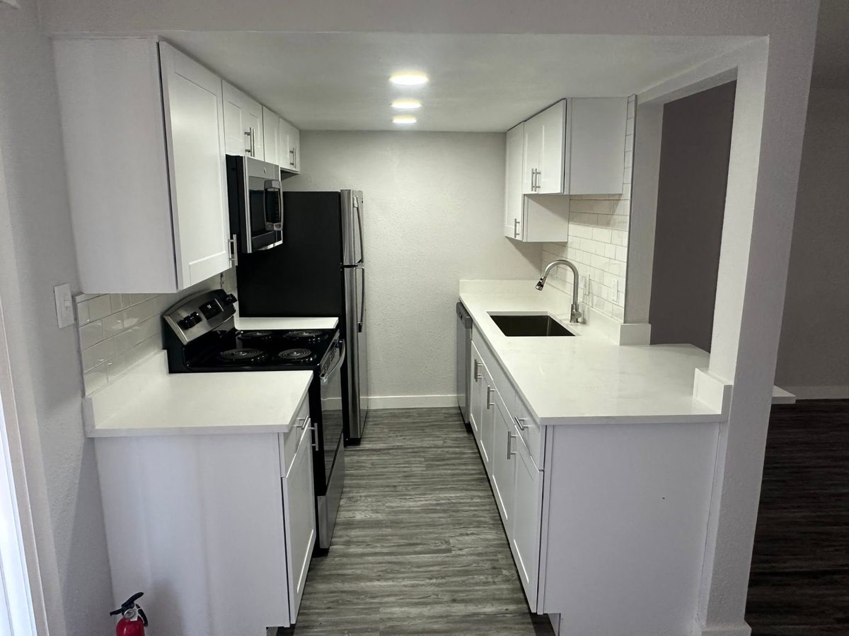 Galley kitchen with white stone counters, white cabinets, and a stainless sink.