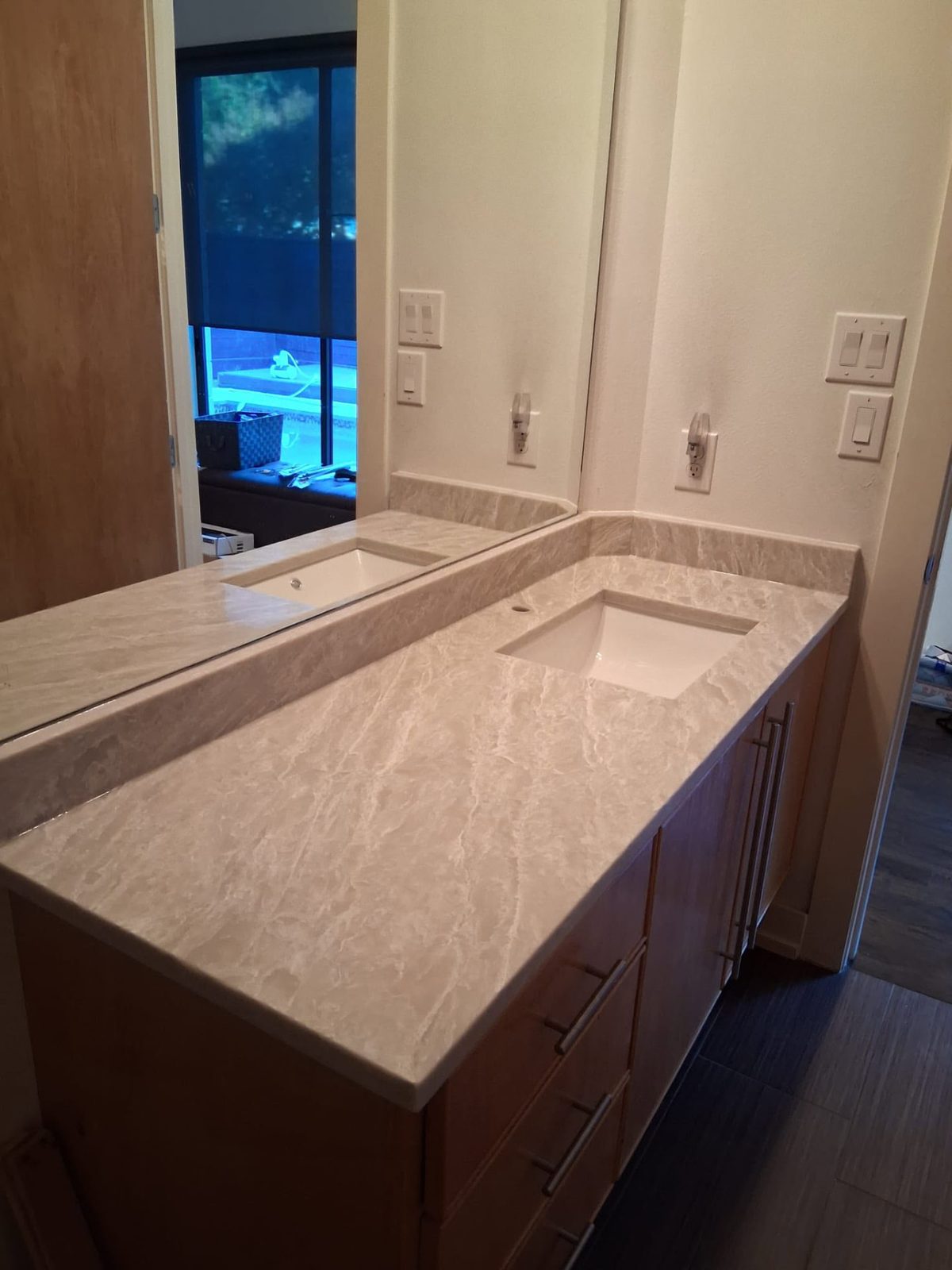 Long double vanity in cream marbled stone with backsplash and undermount sinks.