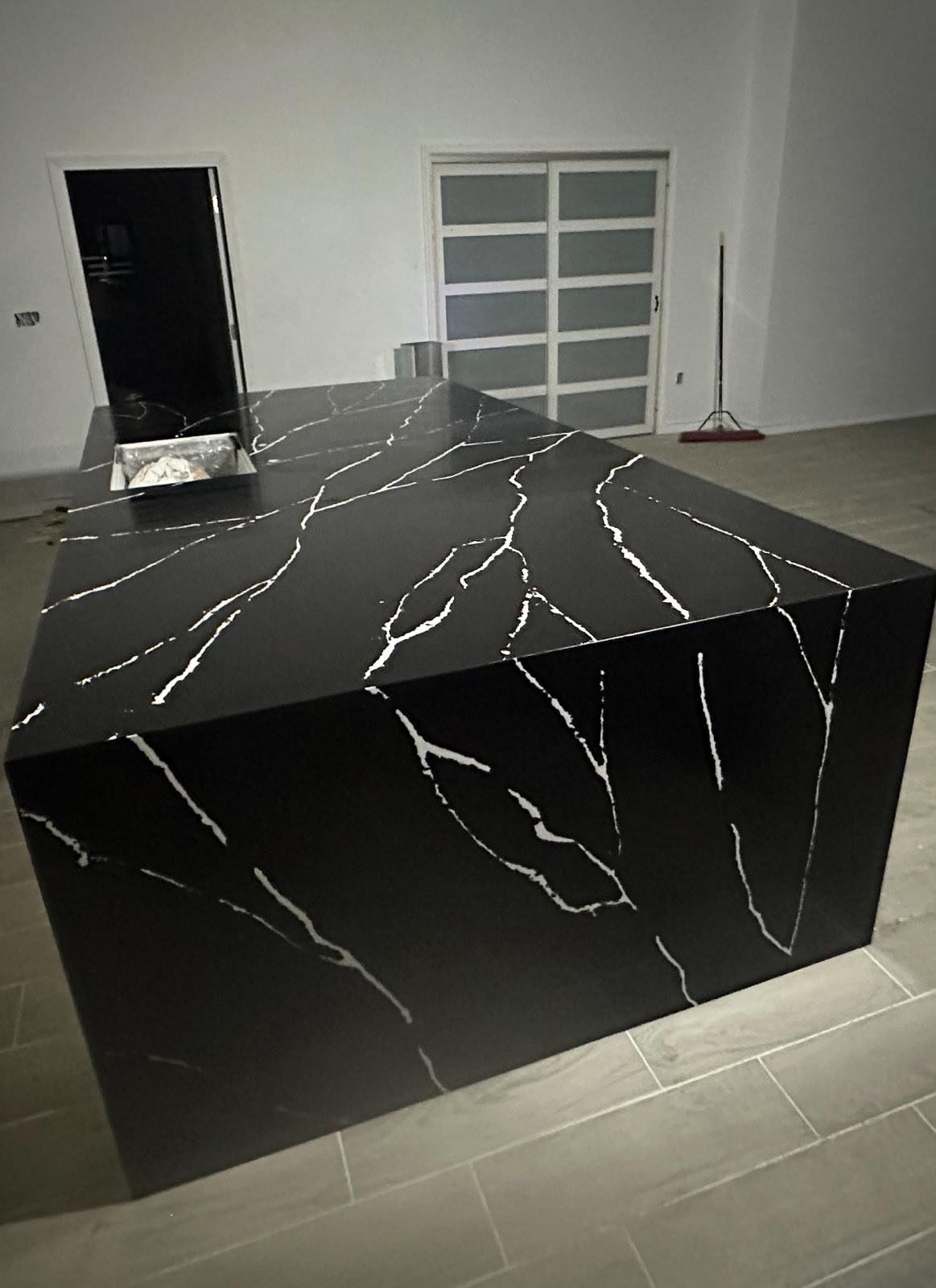 Black stone waterfall island with white veining in a kitchen under construction.