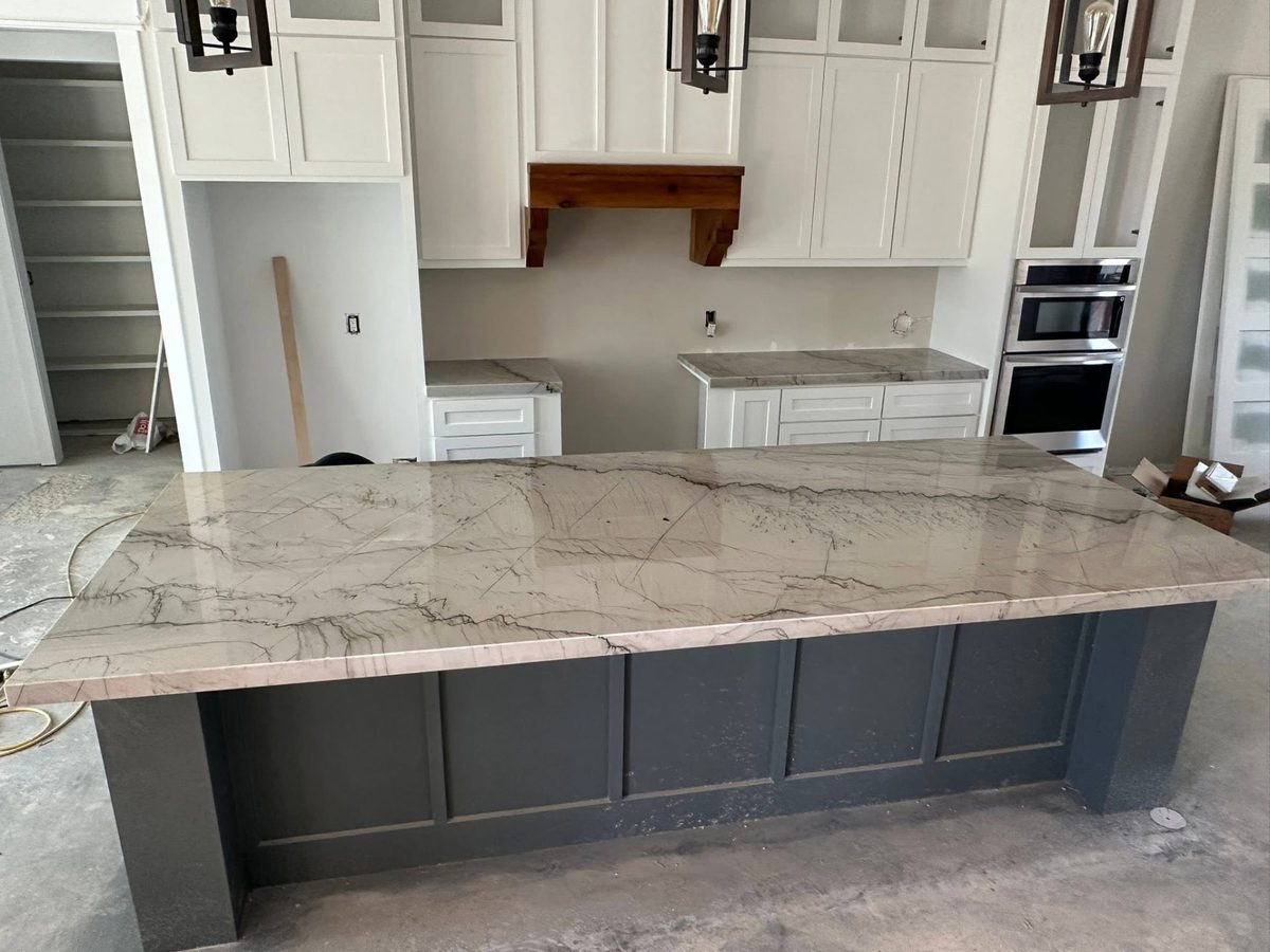 Kitchen island topped with white marble with grey veining on a dark blue base.